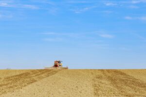 Red tractor sows grain with a seeder on a field in hilly terrain.